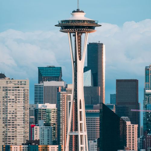 The Space Needle rises above a downtown skyline with tall buildings and a blue sky, Seattle&rsquo;s iconic view.