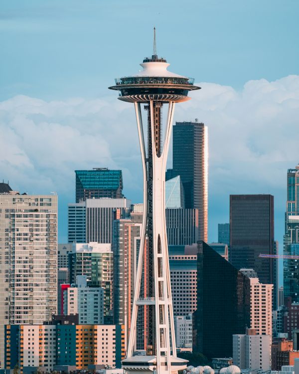 The Space Needle rises above a downtown skyline with tall buildings and a blue sky, Seattle&rsquo;s iconic view.
