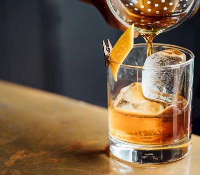 a cocktail is being strained into a glass with ice and an orange peel