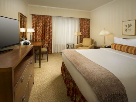 A hotel room with a large bed, nightstands, a seating area, desk, flat-screen TV, and warm beige d&eacute;cor with curtains and framed art, cozy and tidy.