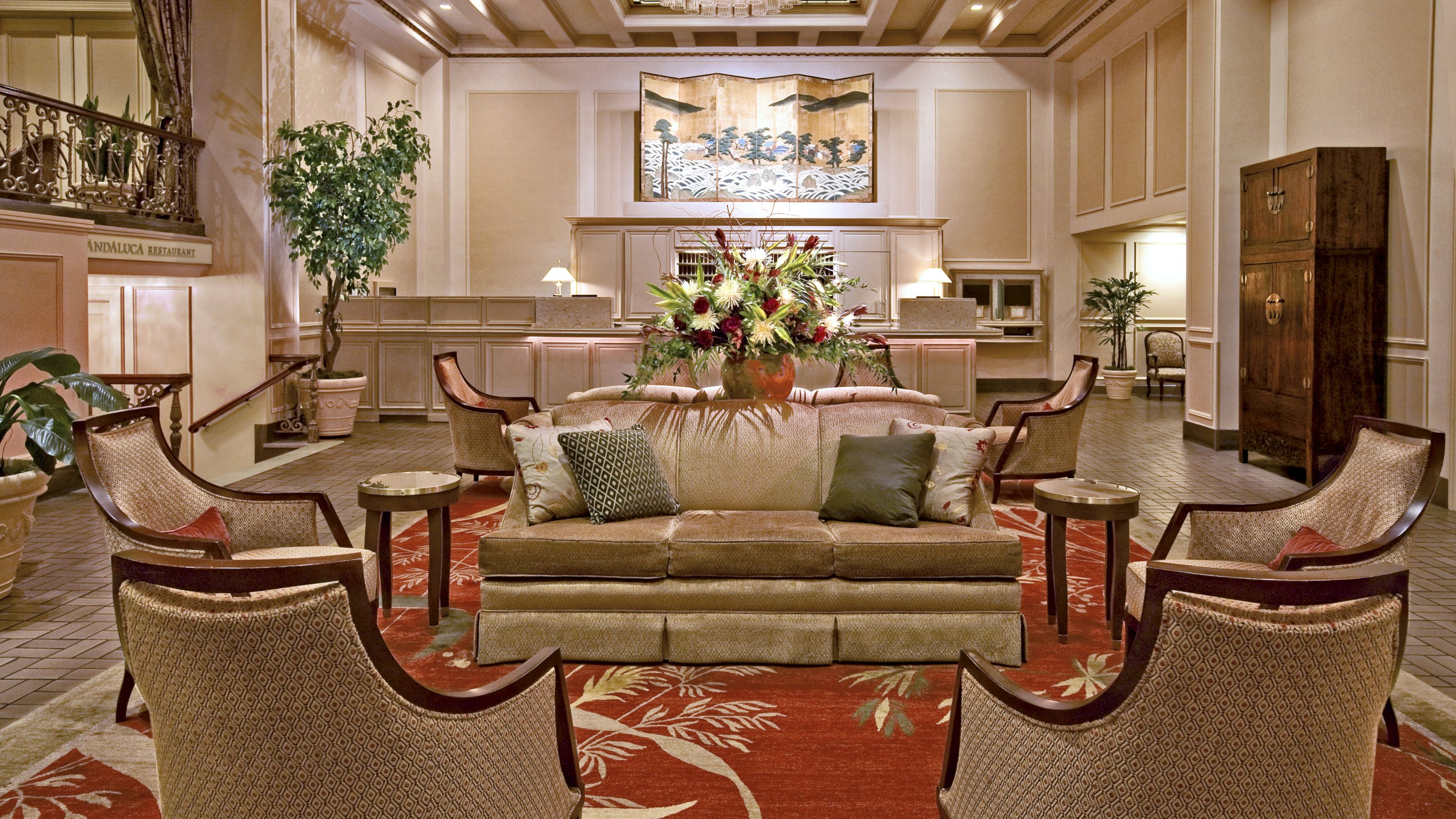 A spacious hotel lobby with a sofa, armchairs, and a coffee table, surrounded by plants and artwork.