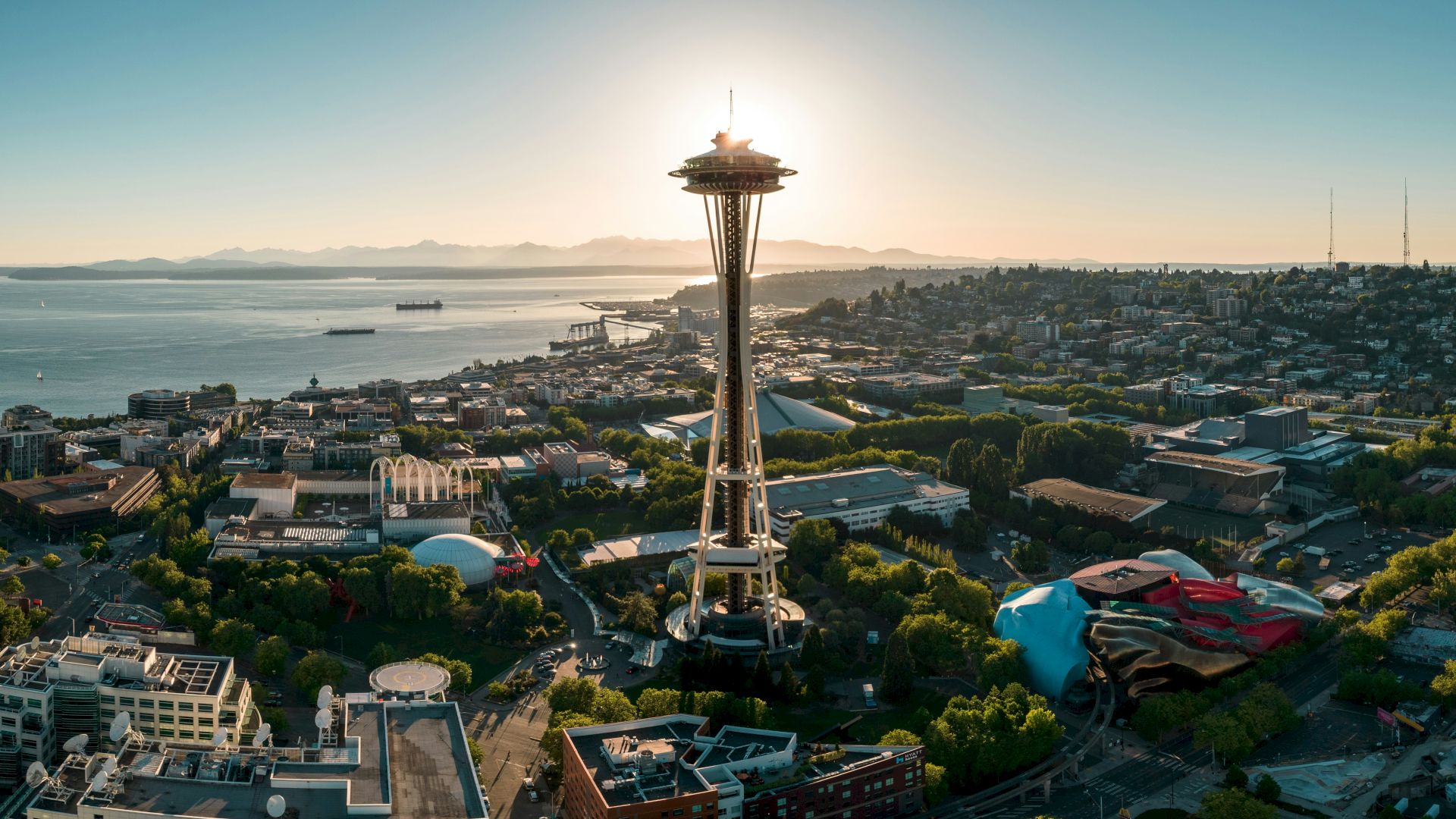 Aerial view of Seattle with the Space Needle towering over downtown, river, and waterfront at sunset, cityscape, greenery, and calm waters.