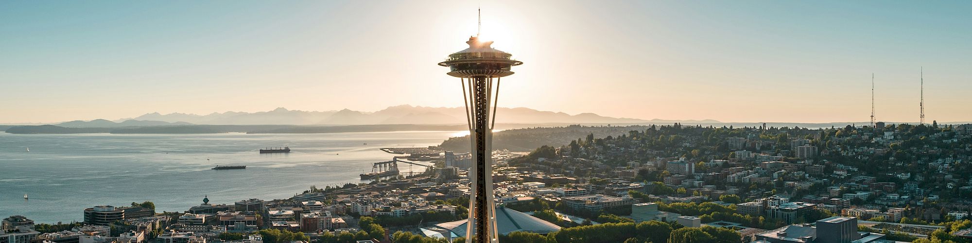 Aerial view of Seattle with the Space Needle towering over downtown, river, and waterfront at sunset, cityscape, greenery, and calm waters.