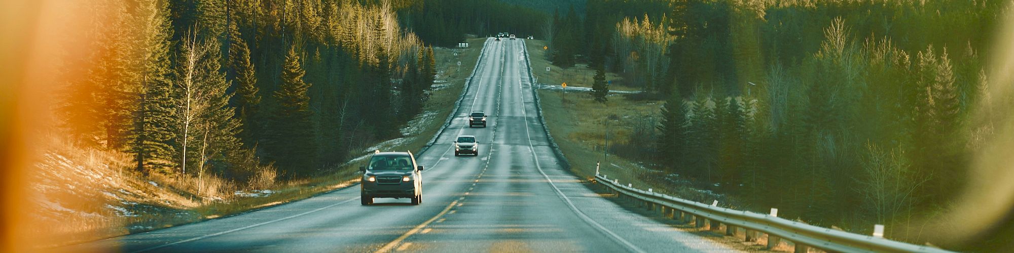 A scenic road through a forested valley with mountains in the distance, cars driving along a long, straight highway.