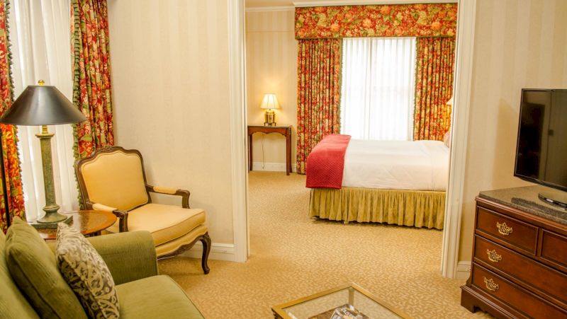 A wide view of a hotel room with a bed, sofa, armchair, TV, and coffee table.