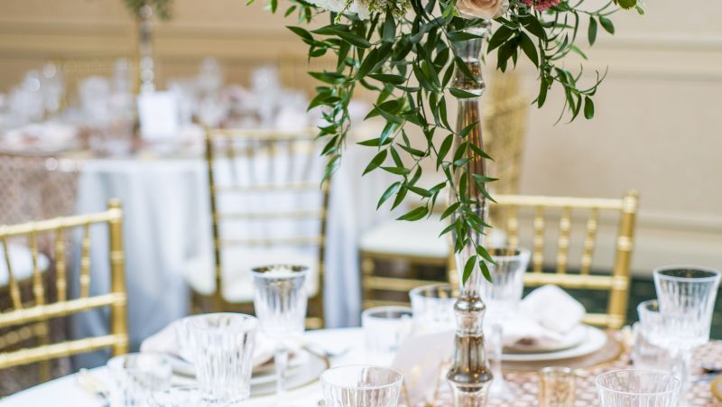 A formal dining setting with a table set for a meal, featuring gold chairs, white tablecloth, and floral centerpieces.