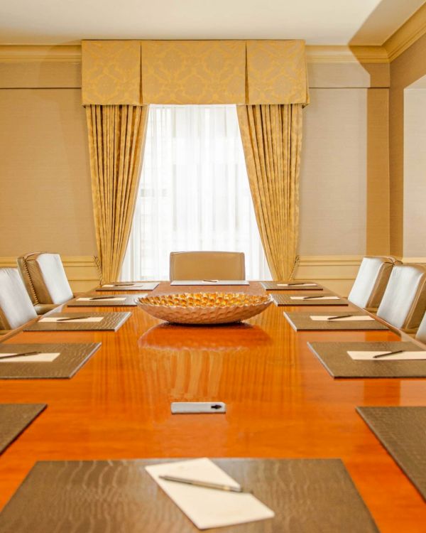 A long, polished wooden conference table with leather chairs, notepads, pens, and a centerpiece in a formal boardroom setting.