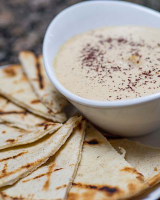 Delicious-looking flatbread with a creamy dip sprinkled with paprika, served on a white plate.