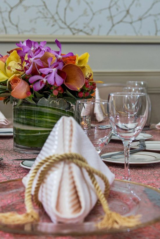 A formal table setting with folded napkins, glassware, and a floral centerpiece arranged for a dinner party.