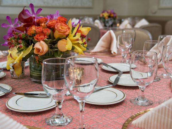 A formal dining table set with plates, utensils, glasses, and a vibrant floral centerpiece, ready for a meal.