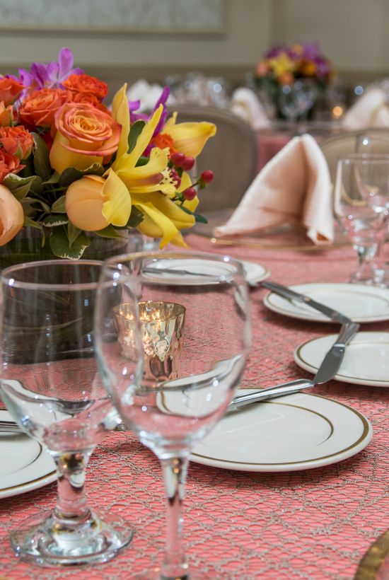 A formal dining table set with plates, sparkling wine glasses, utensils, napkins, and a vibrant flower centerpiece for a fancy meal.
