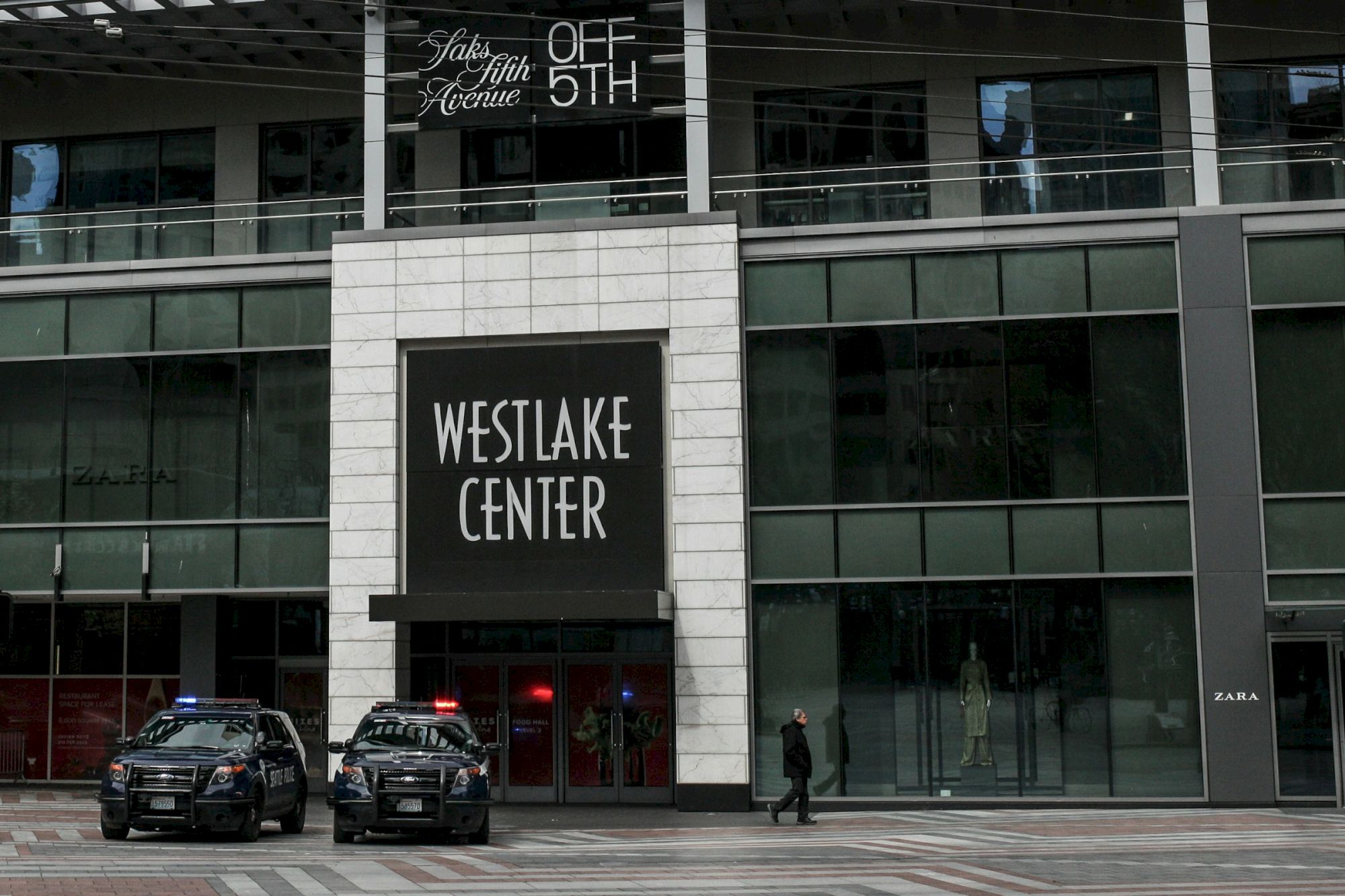 A modern building with a sign that reads &ldquo;WESTLAKE CENTER&rdquo; above the entrance, glass windows, and two parked cars in front.