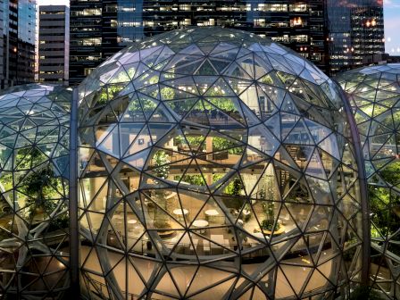 A cluster of glass geodespheres forming a futuristic courtyard in a cityscape at dusk, with lights glowing inside.