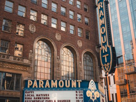 A brick Paramount Theatre facade with a tall vertical marquee, classic sign, and an ornate entrance; theater vibes in downtown cityscape.