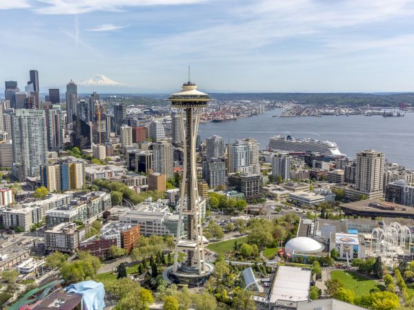 Aerial view of Seattle skyline centered on the Space Needle, with waterfront, bridges, and cluster of high-rises stretching toward Elliott Bay, sunny day.