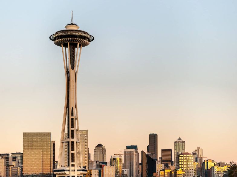 A skyline view of Seattle featuring the iconic Space Needle rising above modern buildings at sunset.