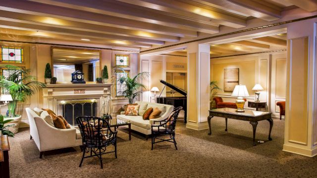 A wide view of a hotel lobby with a fireplace, sofa, armchairs, coffee table, and piano.