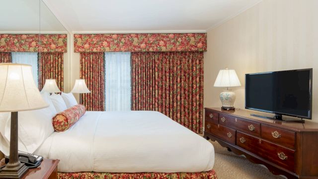 A hotel room with a large bed, dresser, and TV