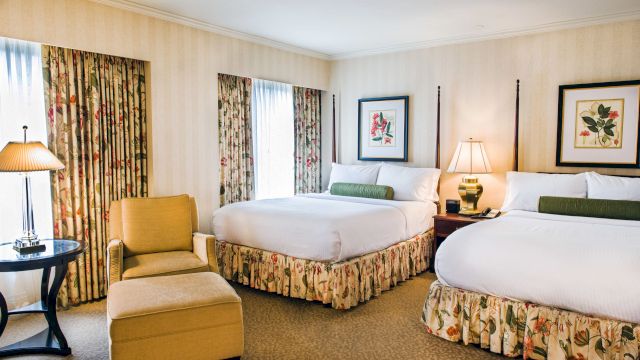 A hotel room with two beds, a chair, and a small table.