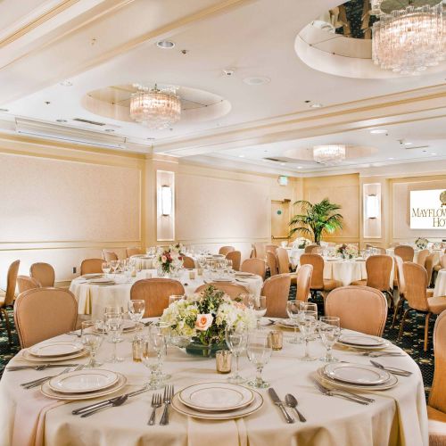 A bright, elegant banquet hall filled with round tables, floral centerpieces, and guests dining under warm lighting, festive and celebratory.