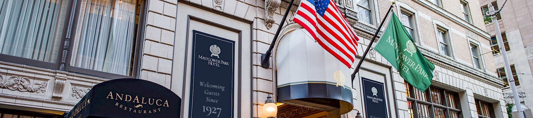 A hotel entrance on a city street with flags (American and green flag) and a curved doorway under a blue sign.