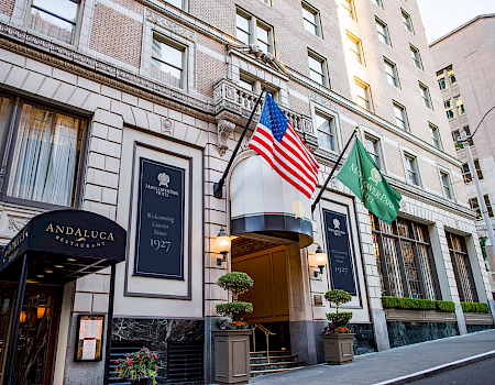 A hotel entrance on a city street with flags (American and green flag) and a curved doorway under a blue sign.
