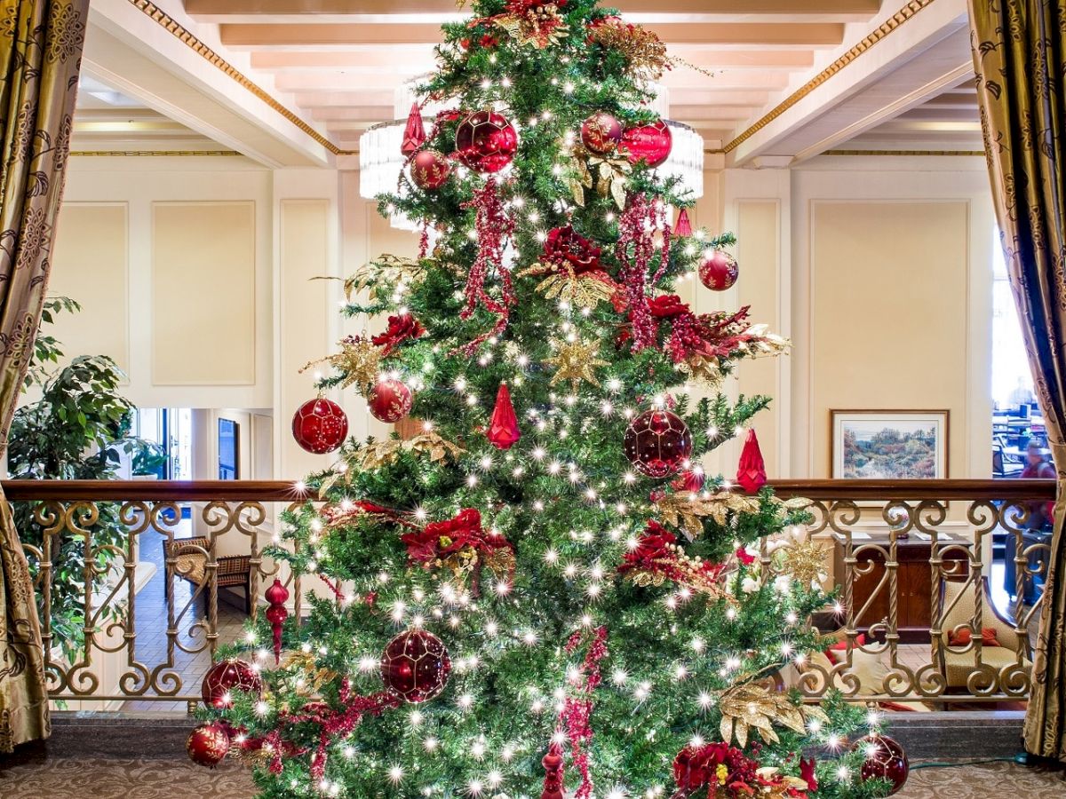 A decorated Christmas tree with red ornaments, twinkling lights, and wrapped gifts beneath in an elegant indoor setting.