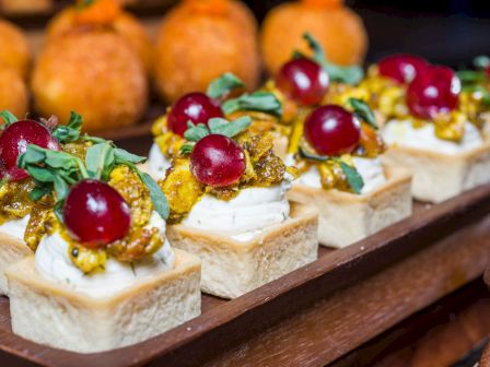 Mini savory bites: cream, toasted nuts, herbs, and cherry on small pastry squares, arranged on a tray for a fancy appetizer.