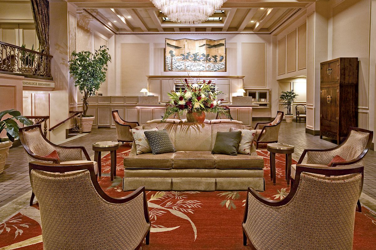 A luxurious hotel lobby with a plush seating area, floral centerpiece, warm lighting, and elegant decor. Top it at 140 characters, always ending the sentence.