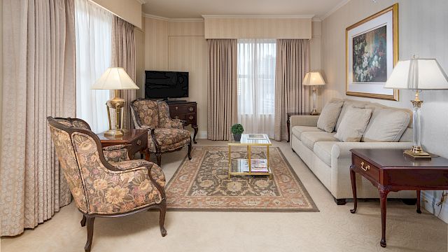 A hotel lobby with a sofa, coffee table, armchairs, lamps, TV, and artwork.