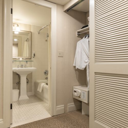 A narrow bathroom or hallway with beige walls, a sink and mirror at the far end, a partially open shower door, and a textured wavy wall panel on the right.