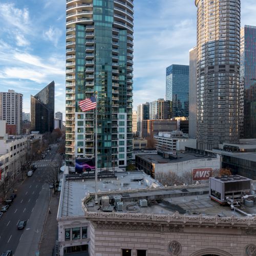 Urban cityscape with tall glass skyscrapers, a mix of modern high-rises and historic buildings, busy streets below under a blue sky.