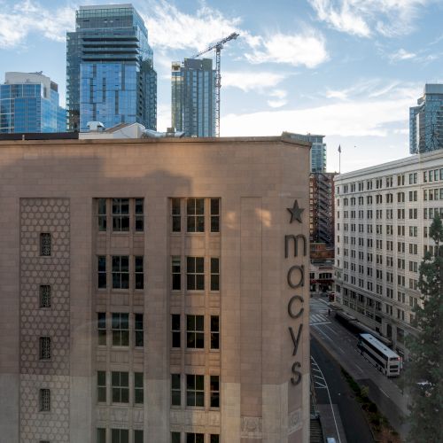 A cityscape view with a mid-rise beige building in the foreground, modern high-rises in the background, and a clear blue sky above.