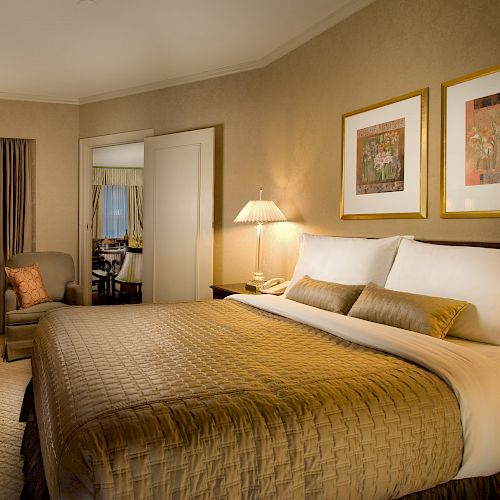 A hotel room with two queen beds, neutral decor, lamps, a desk and chair, a TV dresser, and a seating area near a window.