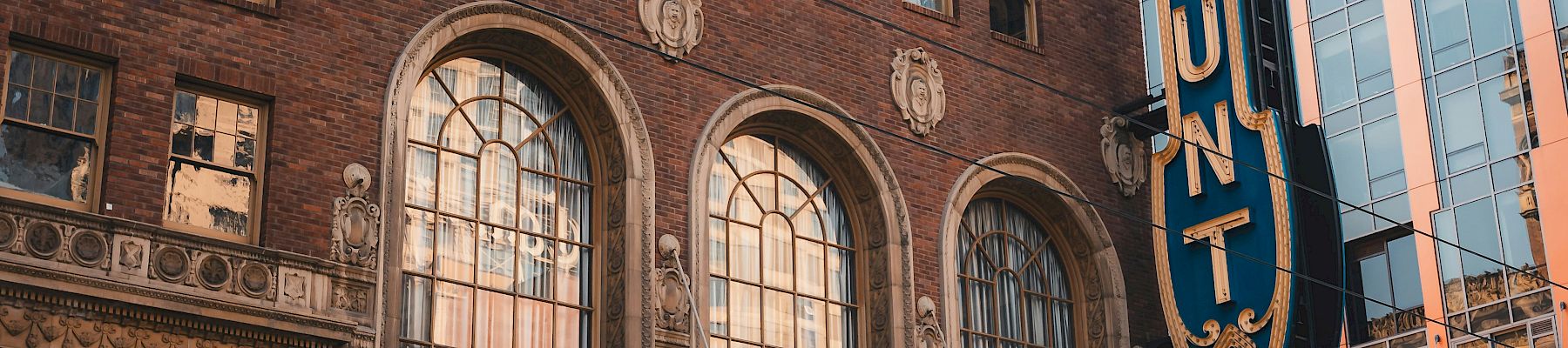 The Paramount Theatre with a tall vertical sign, brick fa&ccedil;ade, and marquee listing show dates. Top it at 140 characters, always ending the sentence.