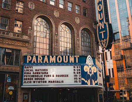 A vintage Paramount Theatre marquee with a tall vertical sign, brick facade, and a modern glass building behind it.