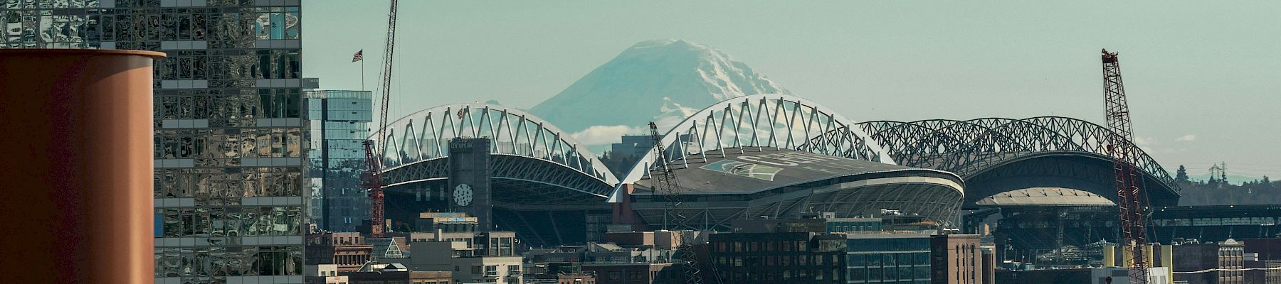 A cityscape with a stadium and cranes, modern buildings, a distant mountain, and a clear sky&mdash;urban construction and landmarks blend together.