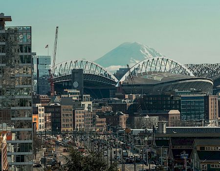 A cityscape with a stadium and cranes, modern buildings, a distant mountain, and a clear sky&mdash;urban construction and landmarks blend together.
